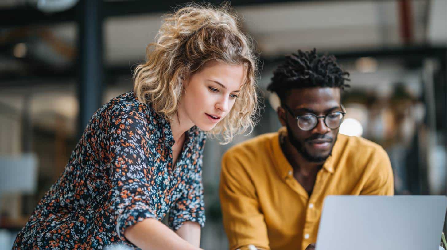 Two marketing professionals reviewing data on a laptop in a modern office, collaborating on B2B marketing analytics strategies.